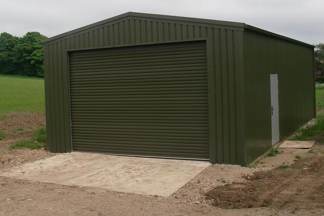 A dark green building with a grey personal access door on the right-hand side